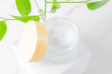 Fototapeta na wymiar A white jar of moisturizing face cream with a bamboolid on a white podium with a plant branch. Cosmetology or skin care concept. copy space, mockup