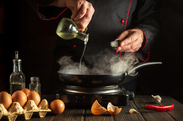 The cook adds vegetable oil while cooking eggs in pan. Work environment on kitchen table. Menu idea for a restaurant or hotel