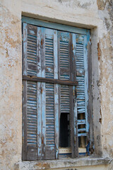 Pale blue weathered shutters on the window of a dilapidated building