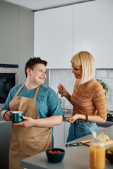 Happy lesbian assists her girlified in tying apron while cooking in kitchen.