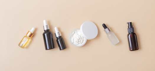 Obraz premium Cosmetic bottle with a pipette and a plastic jar with cream on a beige background. Banner format