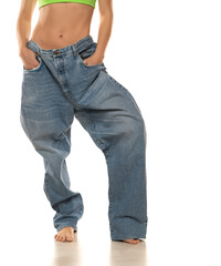 Diet concept and weight loss. Woman in oversize jeans on white background. Close up