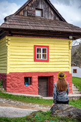 Fototapeta na wymiar Woman sitting and looking on colorful wooden cottage in historical village Vlkolinec at Slovakia