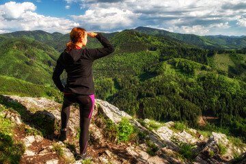 Hiking woman looking from top of the hill on green forest and mountains