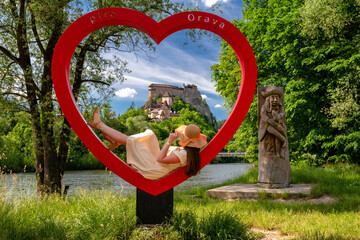 Woman in dress posing in red heart shape and looking on old Orava castle in Slovakia