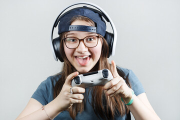 Happy teen girl in headphones and with a gamepad in his hands. Gamer girl playing video games.