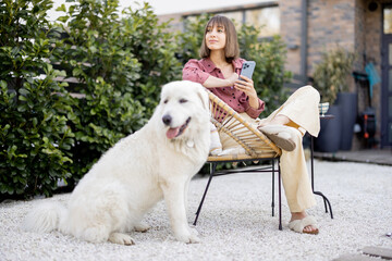Young woman sitting relaxed with her huge white adorable dog, spending time together at backyard. Friendship with pet and happy leisure time outdoors concept