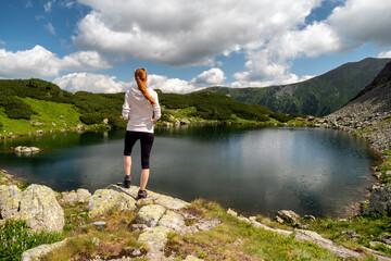 Naklejka na ściany i meble Girl tourist standing and looking on beautiful nature with lake and summer mountains in Western Tatras in Slovakia