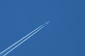 Passenger jet plane flying on high altitude on clear blue sky leaving white smoke trace of contrail behind.