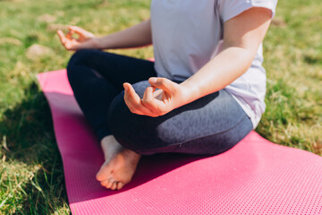 In the lotus posture close up. Woman doing yoga exercises in the summer park. Yoga on grass or sport concept