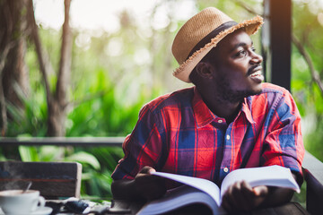 African traveler in a hat with a book and a cup of coffee thinking and looking outside to the view