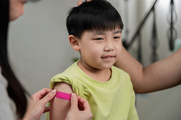 Young Asian mother attaching colorful plaster bandage to her son after received covid-19...