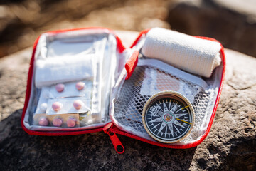 The open bag of the first aid kit lies on a stone. Camping equipment for hiking in the mountains....