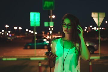 Girl listens to audiobook. Woman with big headphones on blurred background of night city.