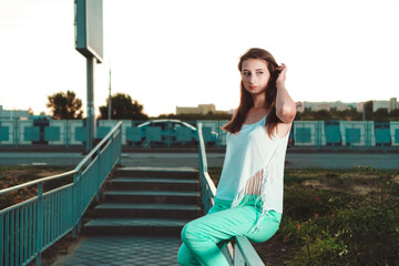 Young woman with long hair sits on handrail. Time before sunset. Spring mood.