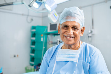 Portrait of senior smiling surgeon at operation theater in gown looking at camera - concept of experienced, expertise and healthcare treatment.