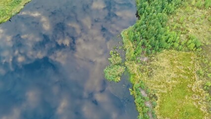 Aerial view of the lake in which fluffy clouds are reflected in the sky. Lonely lake in a swampy area. A beautiful lake far away from civilization.