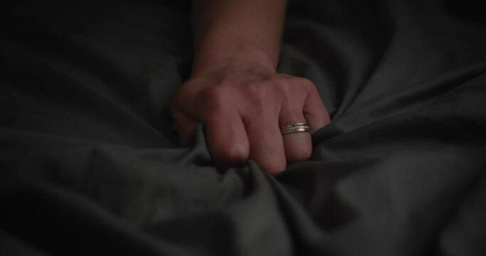 Hands of woman holding on blanket while lying on the bed orgasm sexuality on bed at home. Unknown sexy model girl dreaming about sex pleasure