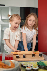 Two little girls siblings having fun and eating on the kitchen at home with japanese food.