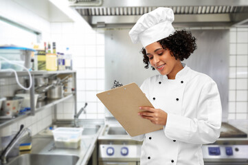 cooking, culinary and people concept - happy smiling female chef in toque and jacket with clipboard...