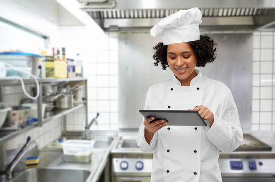 cooking, culinary and people concept - happy smiling female chef in toque and jacket with tablet pc computer over restaurant kitchen background