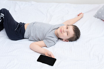 Child boy lying on the bed with smartphone playing games or studying something on it. Social and technology concept