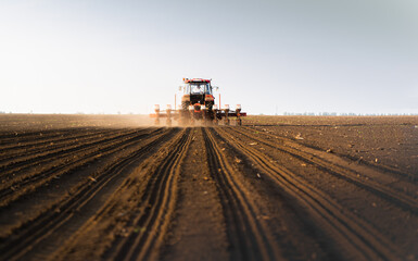 Farmer with tractor seeding - sowing crops at agricultural field