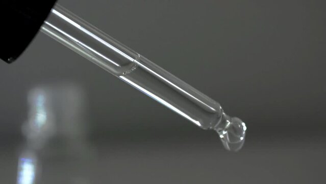 Glass transparent pipette dropper for medical, cosmetic, scientific biology and chemistry laboratory procedures being used by industry professional by dripping liquid water solution droplet
