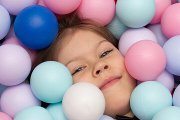 Face of child among multicolor balls on playground inside