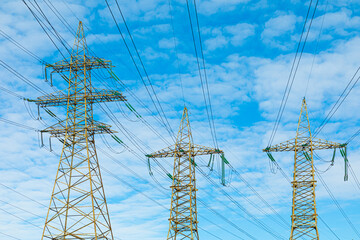 Background, view or scene of steel towers of electric main or electricity transmission line with the wires silhouette on background of cloudy blue sky