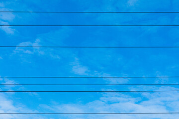 Beautiful bright, vivid and colorful horizontal background or backdrop of blue sky and white clouds with silhouetes of wires of electrical main or transmission line in sunny day
