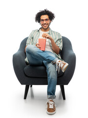 people and furniture concept - happy smiling young man in glasses with popcorn sitting in chair...