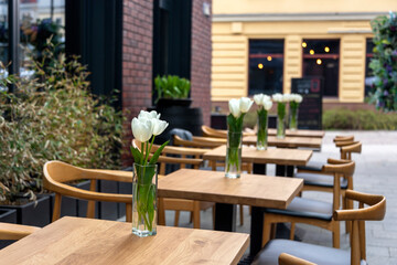 Empty tables with flowers in outdoor cafe or restaurant. Tables and chairs at sidewalk cafe. Touristic setting, tulips on cafe table, sidewalk cafe furniture.