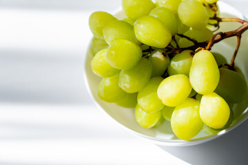 sunshine on green grapes in bowl on white.