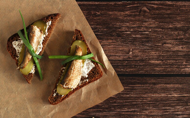brown bread sandwiches with pickles, onions, garlic and sprats on a wooden background