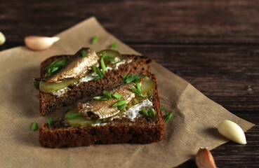 brown bread sandwiches with pickles, onions, garlic and sprats on a wooden background