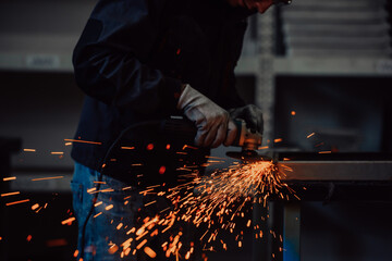 Heavy Industry Engineering Factory Interior with Industrial Worker Using Angle Grinder and Cutting a Metal Tube. Contractor in Safety Uniform and Hard Hat Manufacturing Metal Structures.