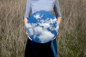 Surrealism with a woman holding a mirror and covering her face in the field with a transparent...