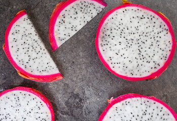 Fototapeta na wymiar Dragon fruit slices on grey mottled surface and ample copy space