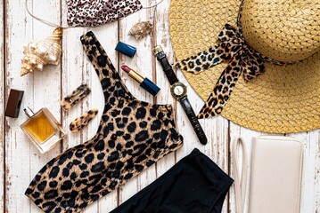 Travel and vacation concept. Flat lay fashion beach holiday accessories with leopard print swimsuit, perfume straw hat, sunglasses and other on wooden background