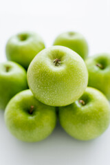 top view of green and ripe apple on blurred pile on white.