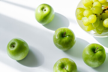 top view of bowl with sweet grapes and ripe apples on white.