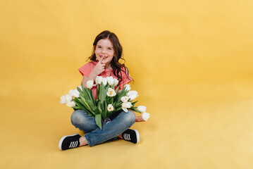 Photo of a cute girl on a yellow background holding a bouquet of white tulips as a gift that she will give to her mother 
