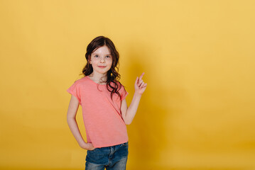 Photo of a cute girl on a yellow background holding , dressed in a pink T-shirt isolated against a yellow background.