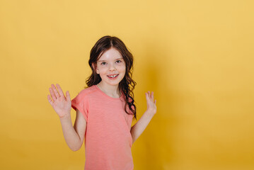 Photo of a cute girl on a yellow background , dressed in a pink T-shirt isolated against a yellow background.
