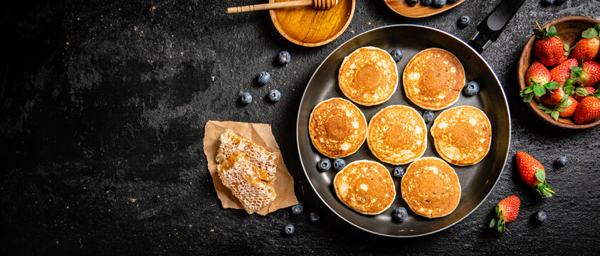 Pancakes in a frying pan with fresh berries and honey. On a black background. High quality photo
