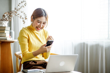 Fototapeta premium Excited happy woman looking at the phone screen, celebrating an online win, overjoyed young asian female screaming with joy, isolated over a white blur background