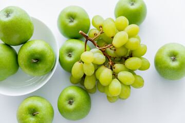 top view of green and ripe apples in bowl near grapes on white.