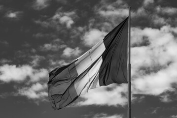 flag on flagpole in a black and white image. Flag waving in the wind on a dark sky with white cloudy