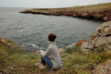 Naklejka na ściany i meble pretty woman in a gray sweater stands on a rocky shore nature Relaxation concept
